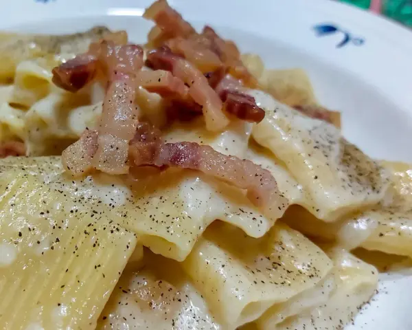 Un piatto di pasta alla gricia fumante, con guanciale croccante e abbondante pepe nero.