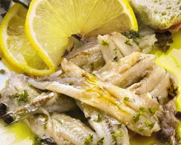 Alici in padella, succulente e dorate, condite con limone fresco, prezzemolo e pepe nero. Un piatto semplice e gustoso.