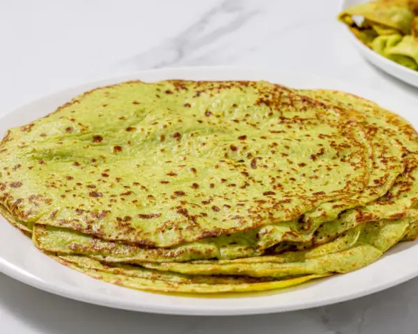 Piatto di crepes di zucchine verdi, sottili e leggermente dorate, impilate su un piatto bianco.