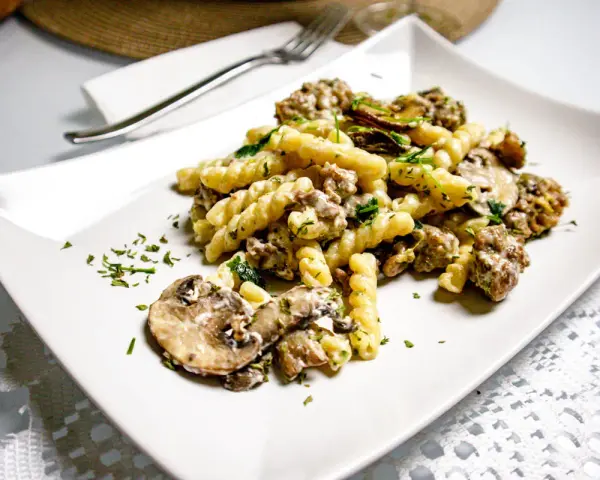 Un piatto di pasta salsiccia e funghi, condito con prezzemolo fresco, servito su un piatto bianco.