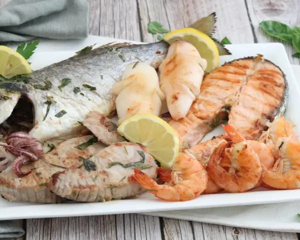 Un piatto invitante di grigliata di pesce: orata intera, tranci di salmone, gamberi, calamari e tonno, guarnito con limone e prezzemolo.