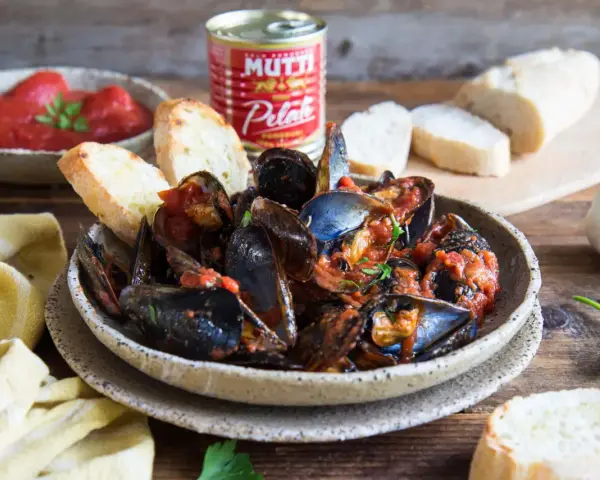Piatto fumante di cozze alla tarantina ricetta, con pane tostato e pomodori pelati Mutti.