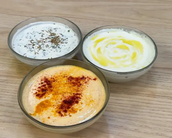 Tre ciotole di salsa con yogurt greco: una con erbe, una con olio d'oliva e una con paprika.