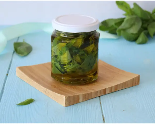 Un vasetto di basilico sott'olio, con foglie fresche sullo sfondo, pronto per insaporire i tuoi piatti.