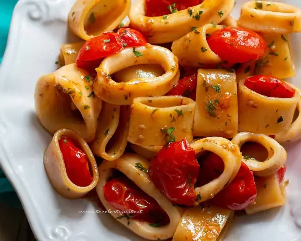 Un invitante sugo di pesce con anelli di calamaro e pomodorini, guarnito con prezzemolo fresco.