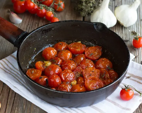 Pomodorini confit in padella, dolci e succosi, cotti con aglio e erbe aromatiche. Un contorno saporito e profumato.