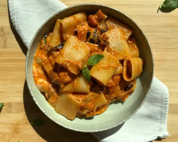 Un piatto di pasta alla siciliana con rigatoni, melanzane e una salsa cremosa al pomodoro, guarnito con basilico fresco.
