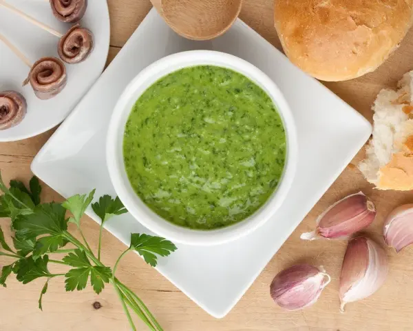 Un invitante bagnetto verde piemontese, accompagnato da acciughe arrotolate, pane fresco e spicchi d'aglio.