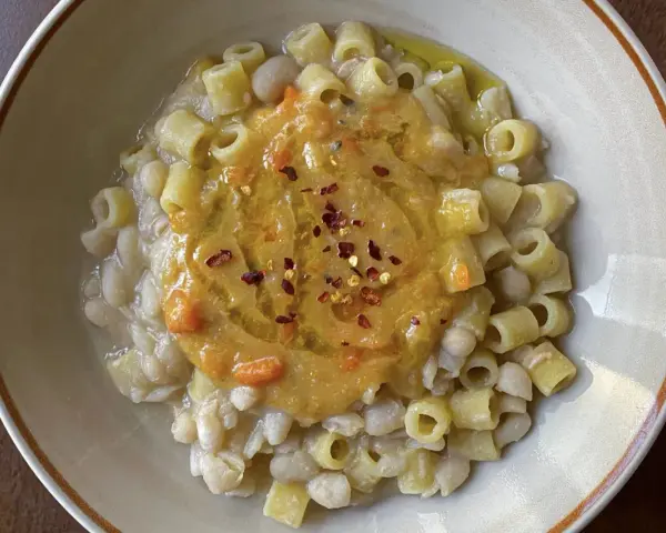 Un piatto di pasta e fagioli estiva, con ditalini e fagioli cannellini, guarnito con una purea di verdure e peperoncino.