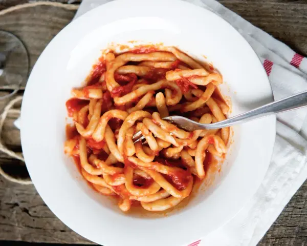 Piatto di pasta fresca condita con un saporito sugo all'aglione, servito su un piatto bianco con una forchetta.