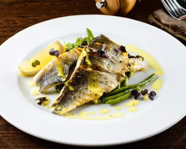Deliziosi secondi di pesce con fagiolini croccanti, limone e una salsa gialla cremosa, guarniti con erbe viola.