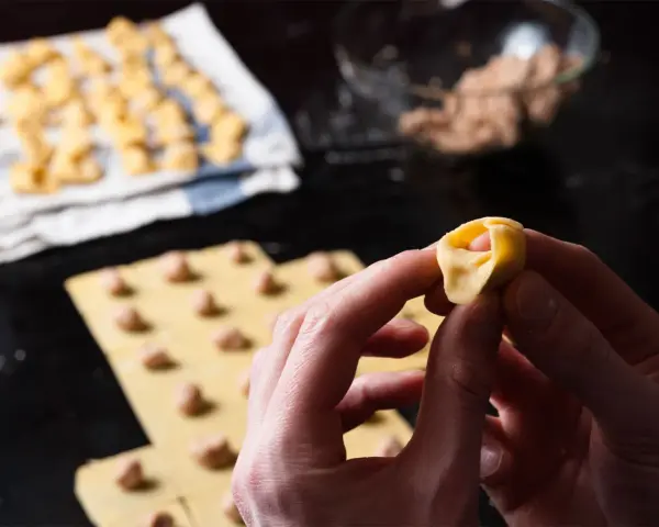 Mani che creano tortellini fatti in casa, con la pasta fresca e il ripieno pronto.