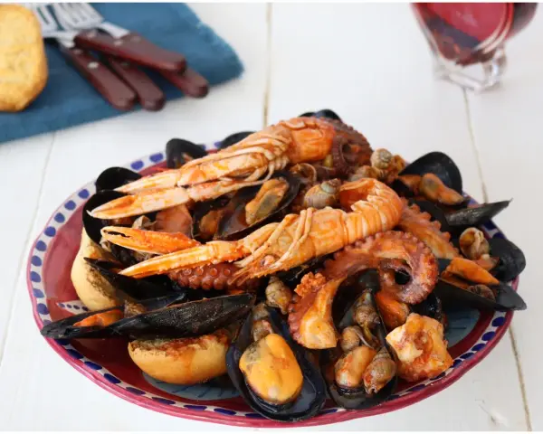 Un piatto ricco di zuppa di cozze, scampi e polpo, servito con pane tostato.