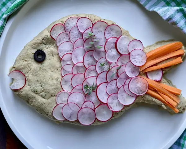 Pesce finto ricetta: un impasto cremoso decorato con ravanelli affettati, carote a bastoncino, un'oliva e erbe aromatiche.