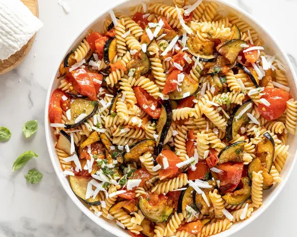 Un piatto invitante di pasta fredda alla norma con melanzane, pomodori e ricotta salata grattugiata.