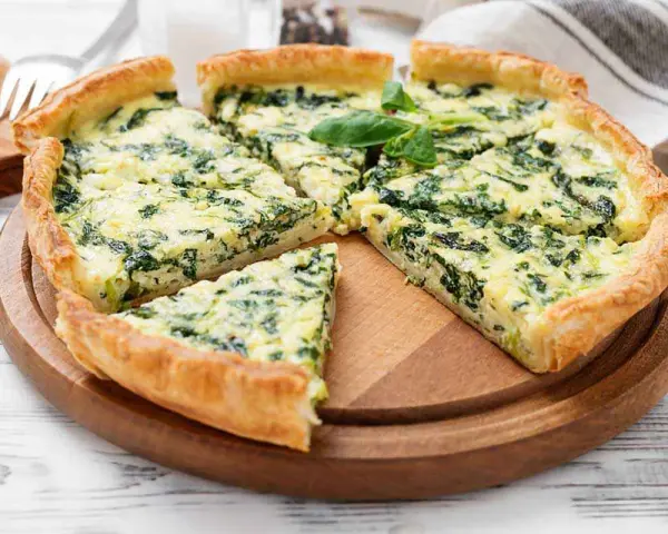 Una fetta di torta rustica ricotta e spinaci, con crosta dorata e ripieno cremoso, guarnita con basilico fresco.
