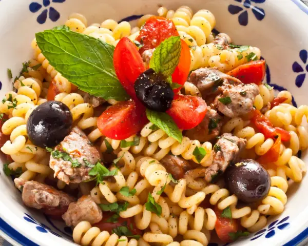 Fusilli con pesce spada, pomodorini, olive nere e menta fresca in una ciotola decorata.