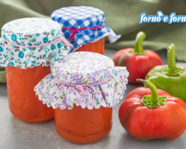 Barattoli di salsa di peperoni fatti in casa, decorati con stoffe floreali e a quadretti, accanto a peperoni freschi.