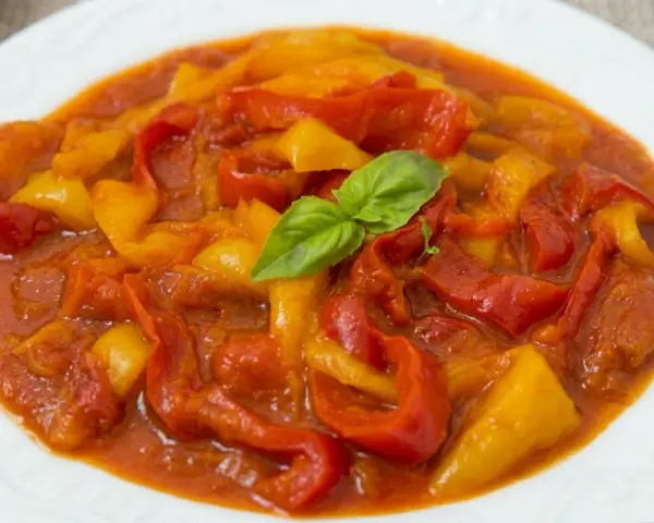 Un piatto di peperonata ricetta, con peperoni rossi e gialli cotti in salsa, guarnito con basilico fresco.