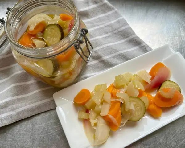 Giardiniera fatta in casa: carote, sedano, cipolle e cetrioli sottaceto in un barattolo e su un piatto. Ricetta facile e gustosa.
