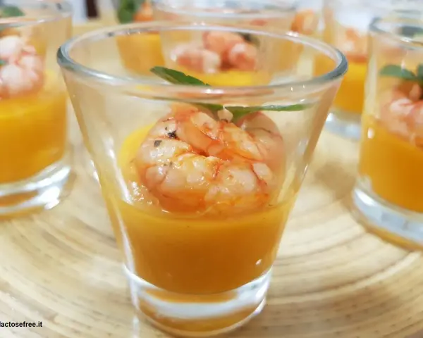 Deliziosi finger food gamberi su crema arancione in bicchierini, guarniti con menta.
