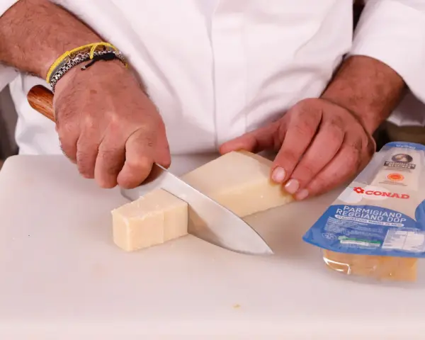 Mani che tagliano un pezzo di Parmigiano Reggiano, pronto per una deliziosa fonduta.