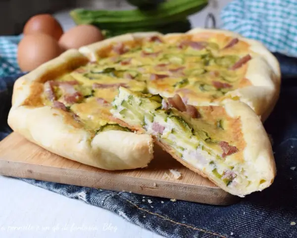 Torta salata con zucchine e pancetta, una fetta tagliata mostra il ripieno gustoso. Ingredienti freschi e profumati.