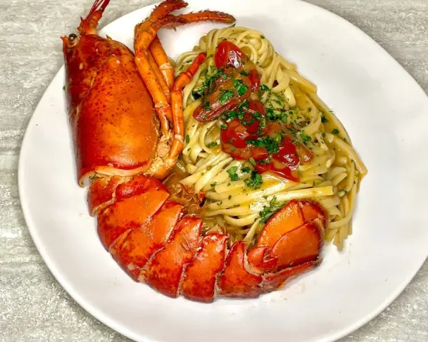 Un piatto di linguine all'astice, con pasta condita e astice intero, guarnito con pomodorini e prezzemolo.