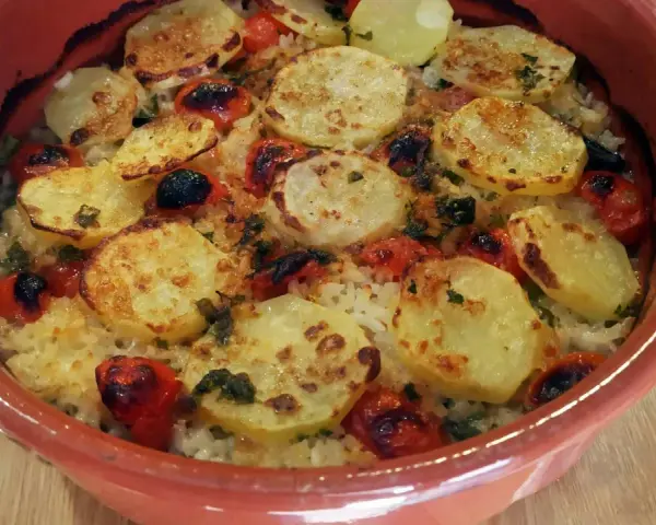 Piatto di riso patate e cozze cotto al forno, con pomodorini e erbe aromatiche, servito in una terrina di terracotta.