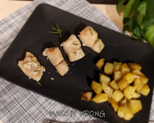 Pezzi di baccalà al forno con rosmarino e patate arrosto su piatto nero.