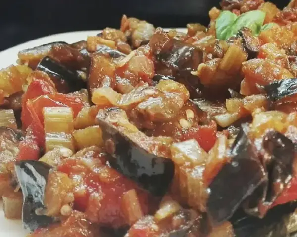 Un primo piano di una saporita caponata siciliana, con melanzane, pomodori e sedano cotti a puntino.