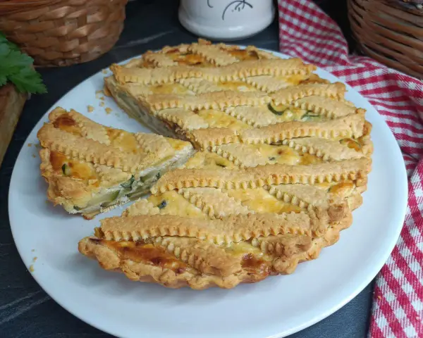 Una deliziosa crostata salata con zucchine e formaggio, con una griglia di pasta dorata e un pezzo tagliato.