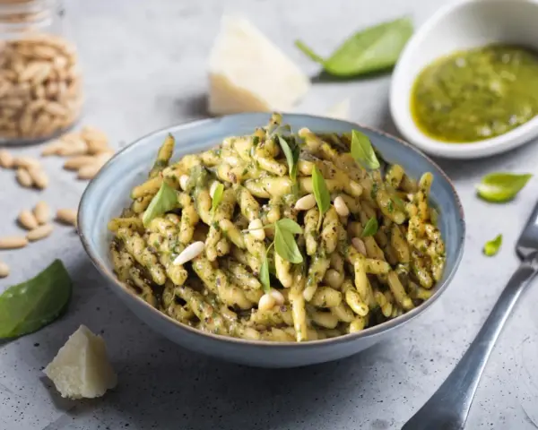 Un piatto di trofie al pesto, condite con basilico fresco, pinoli e parmigiano. Una ricetta classica e gustosa.