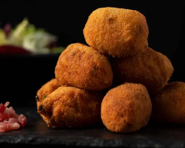 Pile di supplì alla carbonara dorati e croccanti, con guanciale a cubetti e insalata sfocata sullo sfondo.