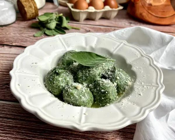 Gnudi verdi, una deliziosa ricetta con spinaci e ricotta, guarniti con parmigiano e una foglia di salvia.