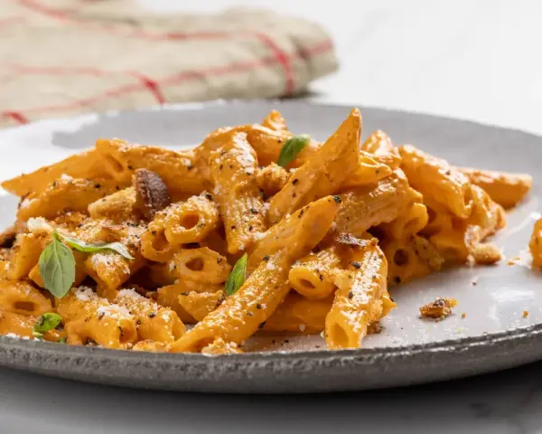 Piatto di pasta con peperoni arrostiti, condita con una cremosa salsa arancione, parmigiano e basilico fresco.