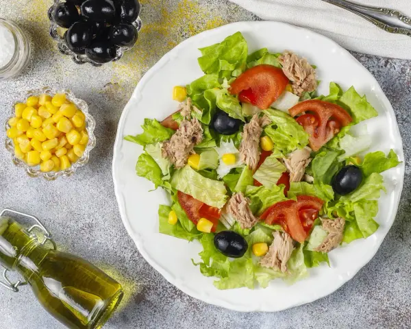 Deliziosa insalata di tonno con lattuga croccante, pomodoro, mais e olive nere. Un piatto fresco e leggero, perfetto per ogni occasione.