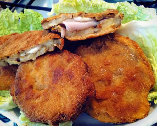 Cordon bleu di melanzane impanati e fritti, ripieni di prosciutto e formaggio filante, serviti su un letto di lattuga croccante.