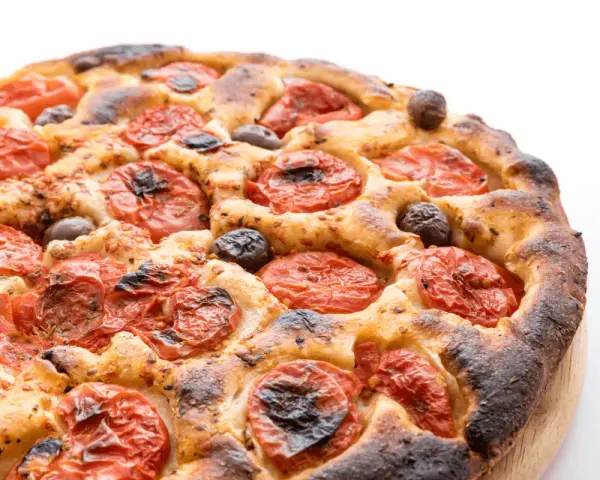 Focaccia barese dorata e fragrante, con pomodorini succosi e olive nere, pronta per essere gustata.