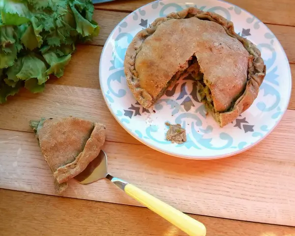 Torta salata con scarola, acciughe e mozzarella, appena sfornata, con una fetta servita su un piatto decorato.
