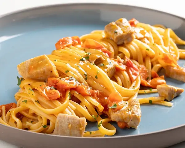 Un piatto invitante di pasta con tonno fresco, pomodorini e prezzemolo, condito con una salsa dorata.