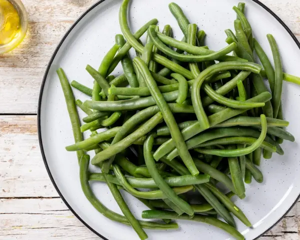 Un piatto di fagiolini lessi, freschi e verdi, pronti per essere gustati. Accanto, un piccolo recipiente con olio d'oliva.