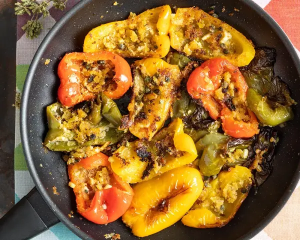 Peperoni ammollicati cotti in padella, ripieni di pangrattato e erbe aromatiche, con colori vivaci.