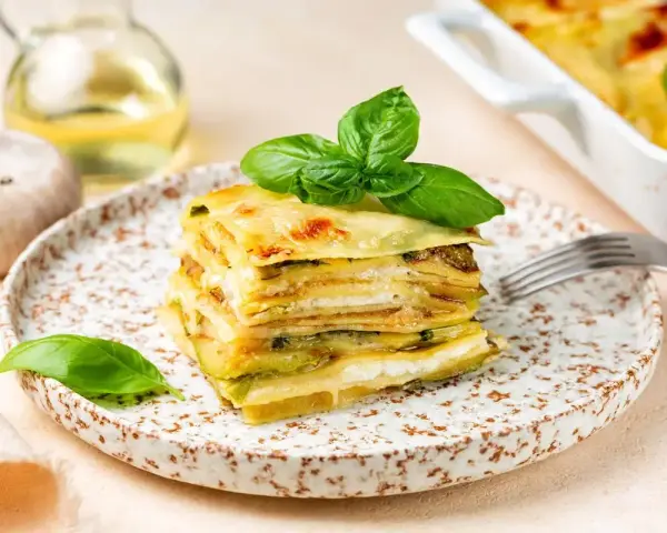 Una fetta di parmigiana di zucchine, stratificata e dorata, guarnita con basilico fresco.