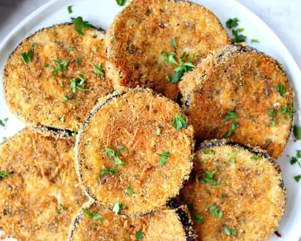 Fette dorate di melanzane impanate al forno, guarnite con prezzemolo fresco. Un antipasto croccante e saporito.