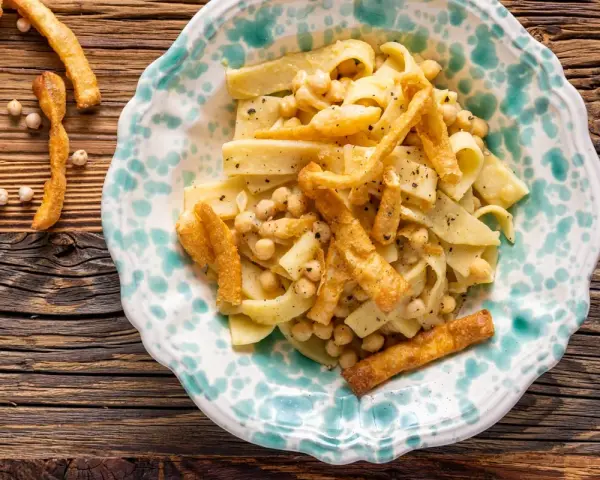 Piatto di ciceri e tria, pasta fresca con ceci e croccanti sfoglie fritte, servito in un piatto decorato.