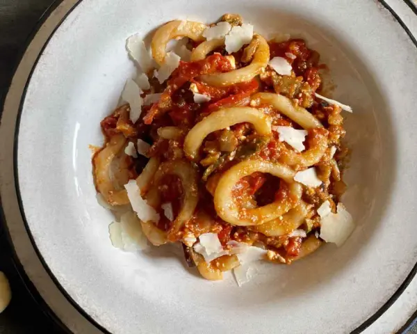 Un piatto di anellini alla pecorara, pasta a forma di anello condita con sugo di pomodoro, verdure e scaglie di formaggio.
