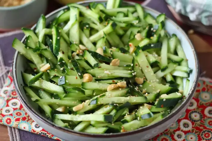 Una ciotola piena di fresca insalata di cetrioli tagliati a julienne, condita con semi di sesamo e arachidi croccanti.