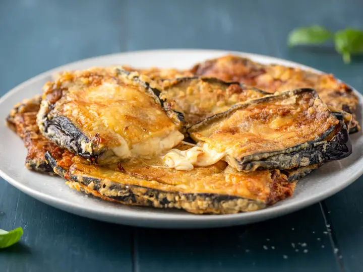 Melanzane contorno dorate e filanti, un piatto invitante con formaggio fuso e basilico fresco.