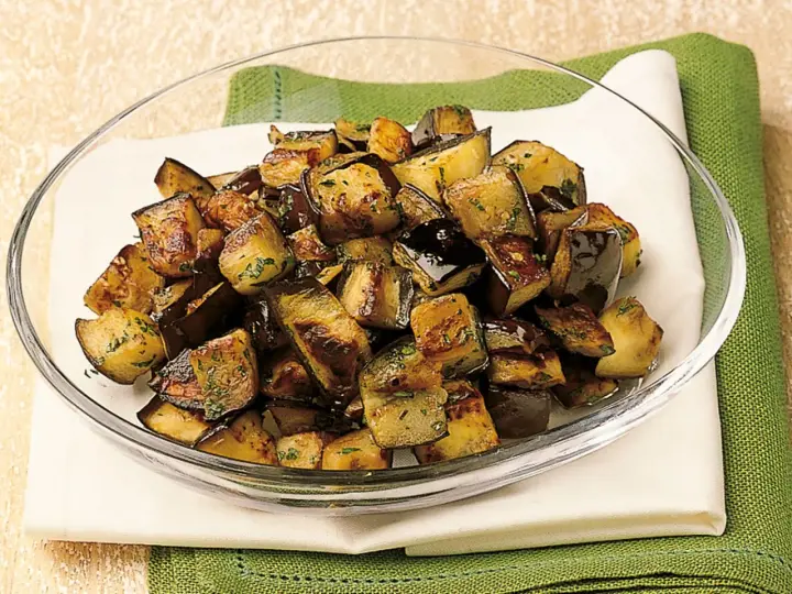 Melanzane a funghetto ricetta della nonna: cubetti dorati e saporiti, conditi con erbe aromatiche, in una ciotola di vetro.